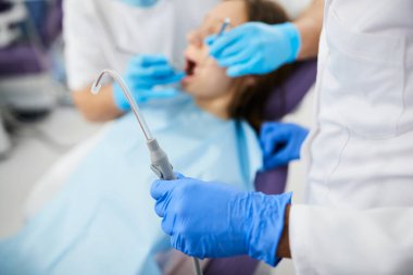 Close-up of orthodontist using dental aspirator for saliva during teeth examination of a patient at dental clinic. 
