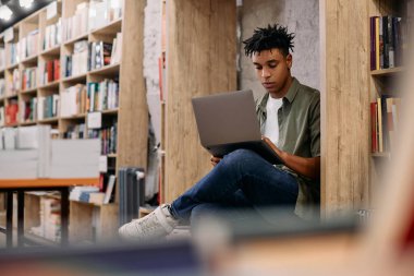 African American student e-learning on laptop during a research in a library.