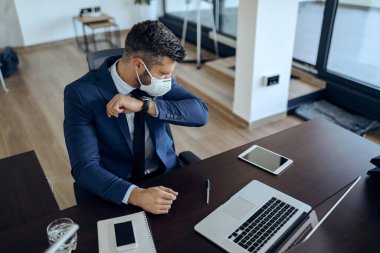 Businessman with protective face mask sneezing into elbow while working in the office. 