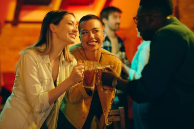 Happy African American woman and her friends having fun while tasting with beer in a bar at night.