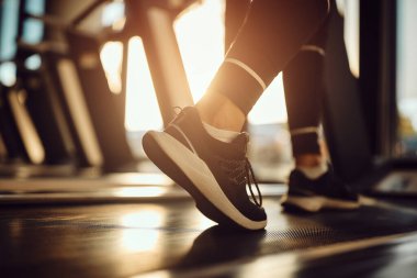 Close-up of athletic woman warming up for sports training while walking on treadmill in a gym.