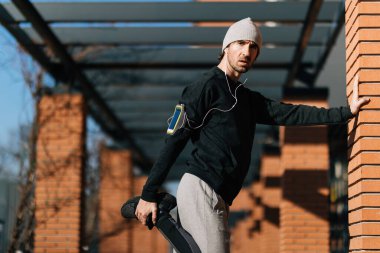 Young athletic man warming up and doing stretching exercises outdoors. 