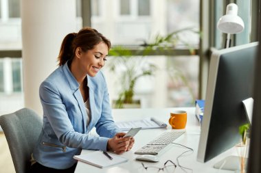 Young happy businesswoman using mobile phone and text messaging while working in the office.