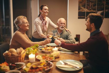 Happy senior couple and their adult children toasting with wine while having family dinner at dining table. 