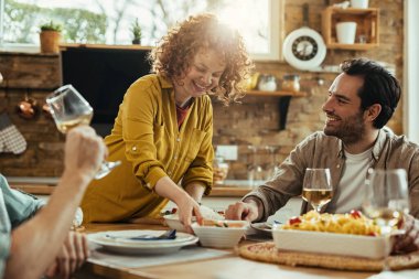 Happy woman bringing food at the table and having fun with her friends during lunch time at home. 