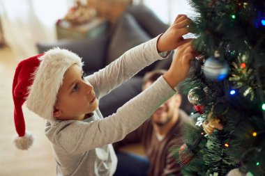 Little boy preparing for holidays and decorating Christmas tree at home. 