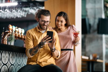 Young happy couple watching something funny on smart phone in a cafe.