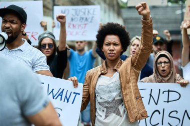 Crowd of people participating in anti-racism protest. Focus is on black woman with raised fist.