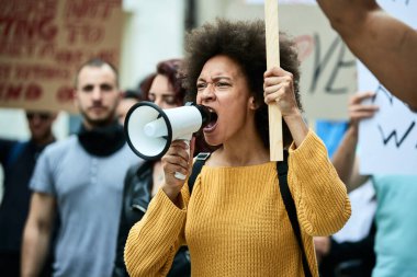 Young African American woman taking a part in a protest for human rights and shouting though megaphone.
