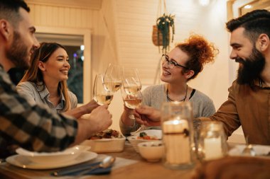 Small group of happy friends having fun while toasting during dinner at home. Focus is on redhead woman. 