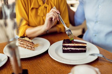 Close-up of unrecognizable couple having dessert and sharing cake in a cafe. 