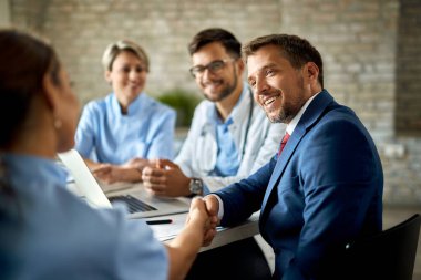 Happy businessman having a meeting with group of doctors and shaking hands with one of them in the office. 