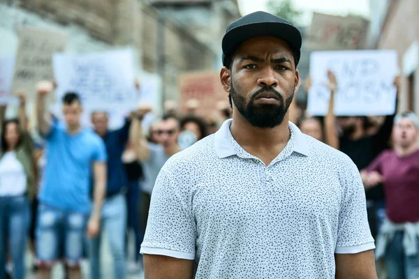 Young black man participating in a protest for human rights and looking at the camera. Crowd of people is in the background.