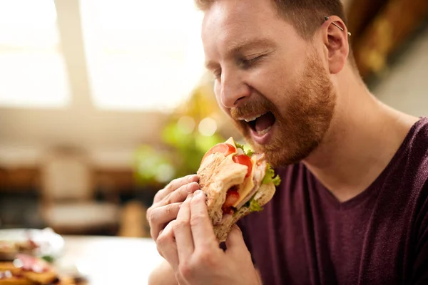 Close-up of man eating sandwich with eyes closed at home.