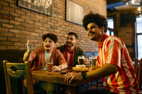Happy Lebanese man and his male friends watching sports game on TV in a bar.