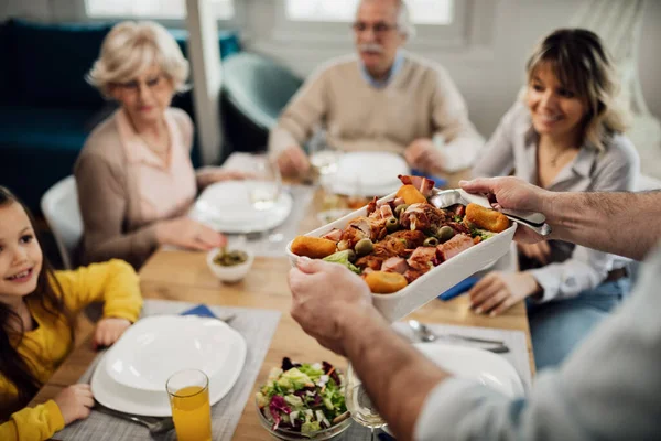 Close-up of man brining food at the table while having lunch with his family at home.