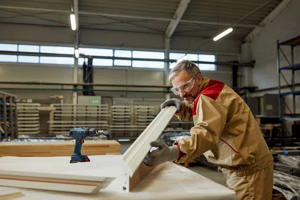 Happy mid adult carpenter analyzing piece of wood while working in a workshop.