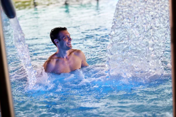 Happy man with eyes closed enjoying at indoor swimming pool at the spa.