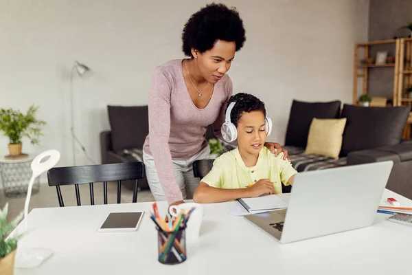 Smiling black mother and son using laptop while doing homework in the living room.