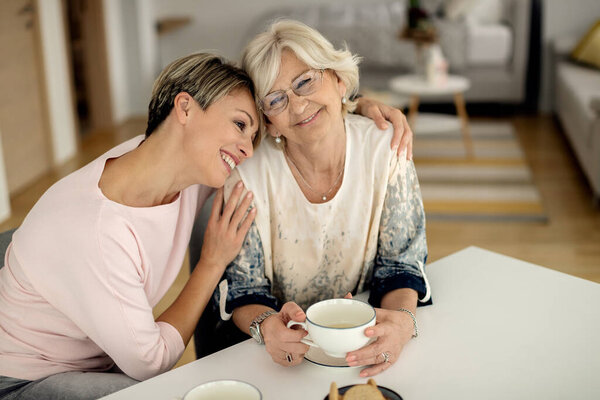 Счастливая взрослая дочь обнимает свою зрелую мать, расслабляясь дома. 