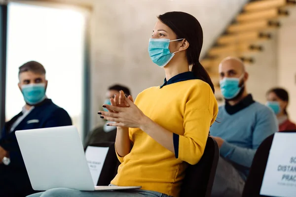 Group of business people with face masks applauding after successful conference in board room. Focus is on a businesswoman in foreground.