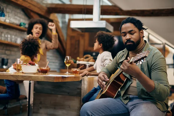 African American Man Playing Acoustic Guitar While His Family Having — стокове фото