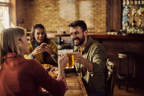 Happy friends toasting with beer while eating in a pub. Focus is on man.