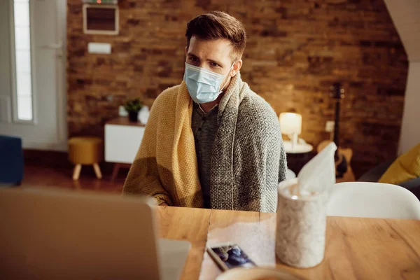 Man with face mask feeling unwell and calling his doctor via video call from home.