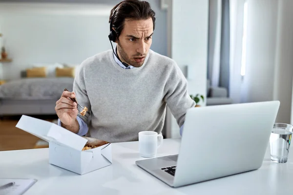 Young businessman using computer while having lunch break at home.