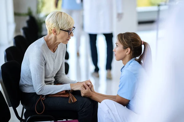 Young Nurse Mature Woman Holding Hands While Talking Waiting Room — Stockfoto