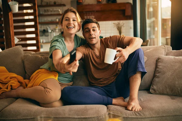 Young man trying to stop his girlfriend not to change the channel while watching TV at home.
