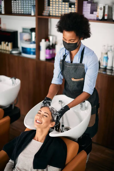 African American Hairdresser Wearing Face Mask While Washing Young Woman — Fotografia de Stock