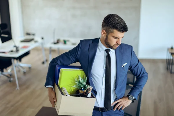 Distraught businessman holding his belongings and feeling worried while getting fired from his job. 