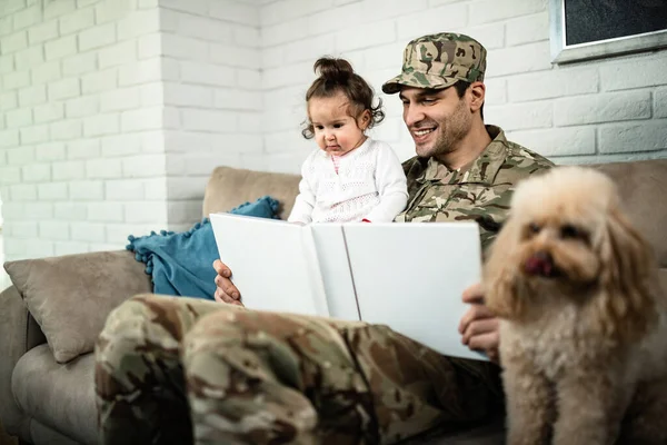 Happy military man enjoying with his small daughter while looking at pictures in photo album and relaxing at home.