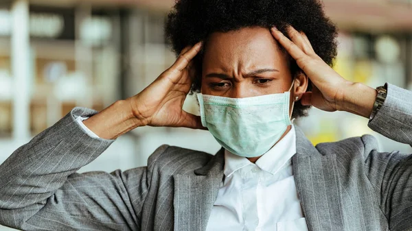 Distraught black businesswoman wearing face mask while feeling frustrated during virus epidemic.