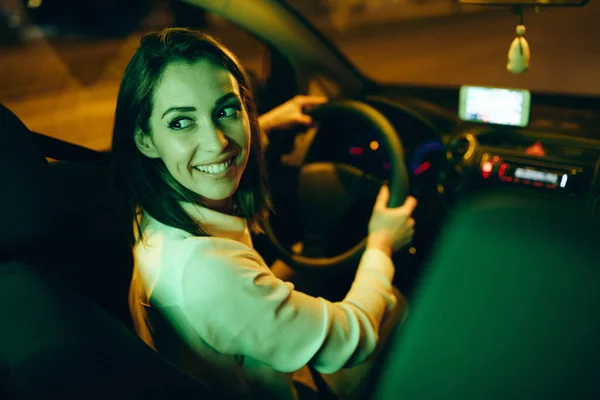 Young happy woman drives car in a reverse at night.
