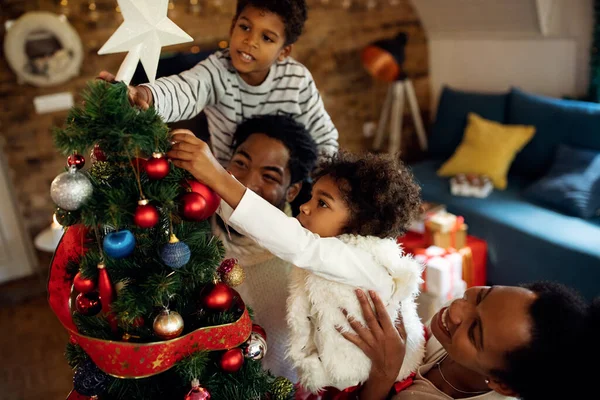 Happy African American children decorating Christmas tree with help of their parents at home.