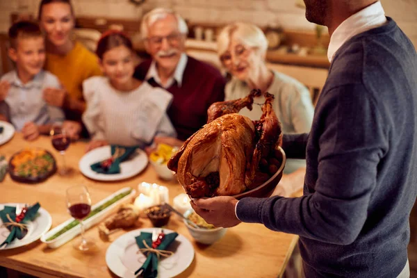Close-up of man serving roast turkey during Thanksgiving lunch with his family at dining table.