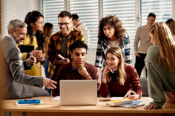 Group of happy students using computer with their professor in the classroom at the university.