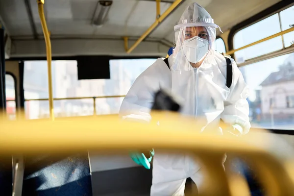 Man in protective suit doing disinfection inside of public bus during coronavirus pandemic.