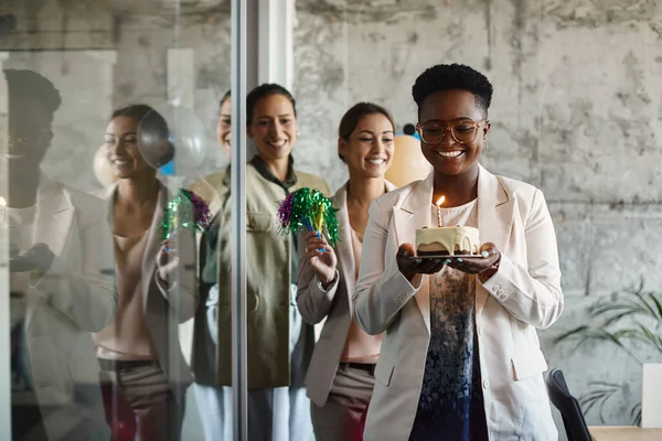 Happy businesswomen celebrating their colleague\'s Birthday in the office. Focus is on African American businesswoman carrying Birthday cake.