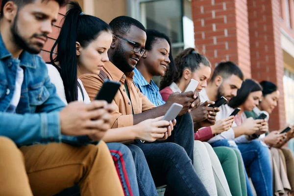 Large group of multiracial group students surfing the net on their smart phones at campus. Focus is on African American male student.