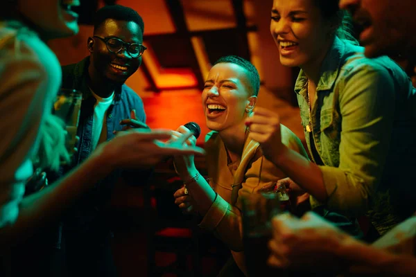 Gece kulübünde arkadaşlarıyla parti yaparken mikrofon tutan ve şarkı söyleyen Afrikalı Amerikalı bir kadın..