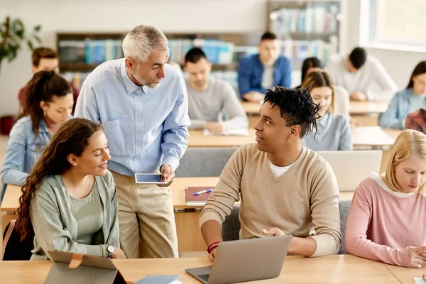 College students communicating with their professor while e-learning on laptop at lecture hall.