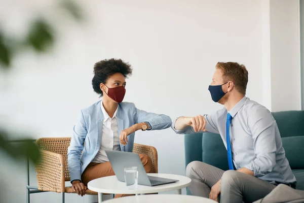 African American businesswoman and her colleague wearing face masks and greeting with elbows in the office. Copy space.