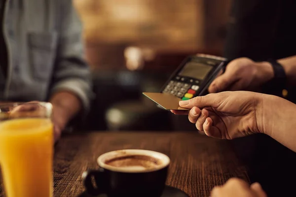 Close-up of guest using credit card while paying bill to waiter in a pub.