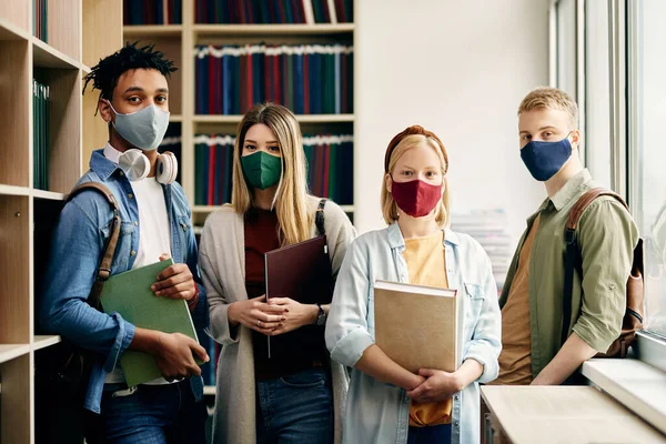 Portrait of university students with face masks studying in library and looking at camera.