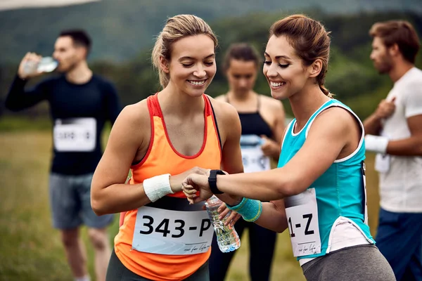 Happy marathon runner showing smart watch to her friend before the race in nature.