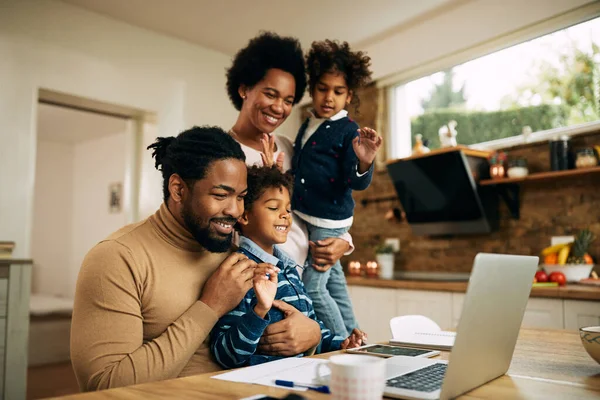 Happy African American parents and kids having video call and greeting someone over a laptop from home.