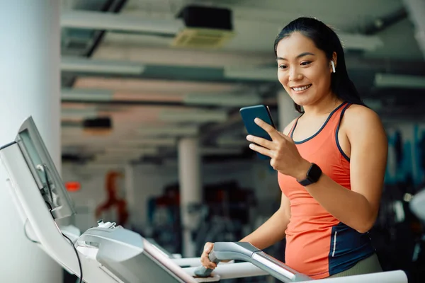 Šťastná Asijská Sportovkyně Textové Mobilu Při Tréninku Běžícím Pásu Tělocvičně — Stock fotografie
